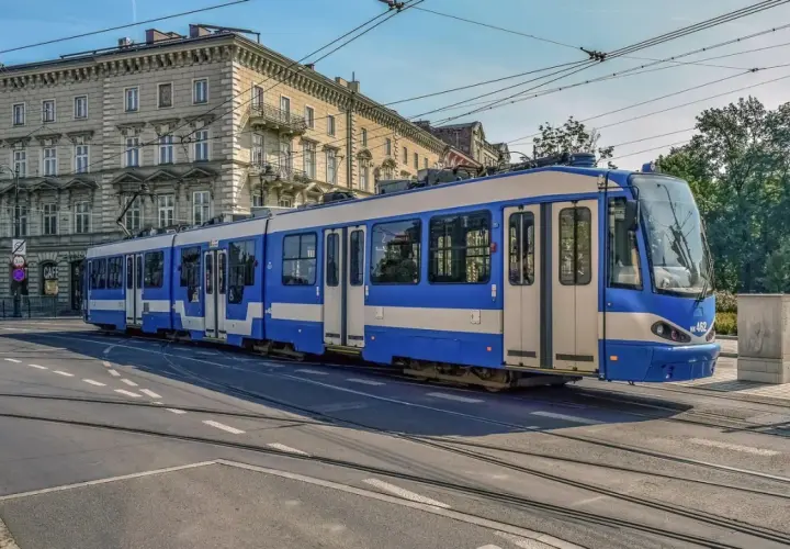Niebiesko-biały tramwaj na torach w Krakowie. To część krakowskiej komunikacji miejskiej, która przewozi pasażerów przez miasto.