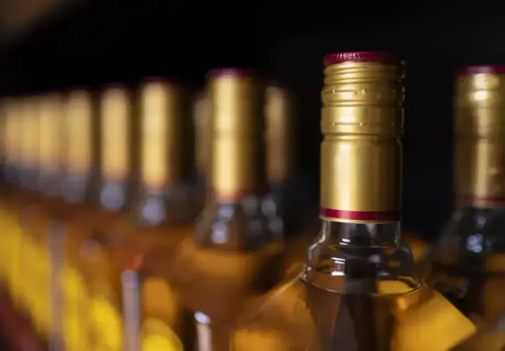 Rząd butelek z bursztynowym płynem, każda z złotą zakrętką i czerwoną obrączką. Zastanawiasz się, ile alkoholu do uk?