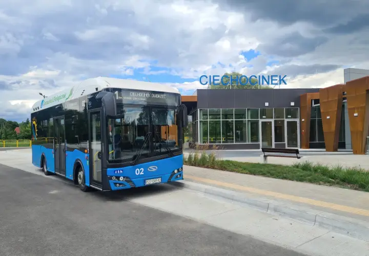 Niebieski autobus ekologiczny z napisem "Ciechocinek Dworzec" czeka na pasażerów. W tle nowoczesny budynek dworca z napisem "Ciechocinek".