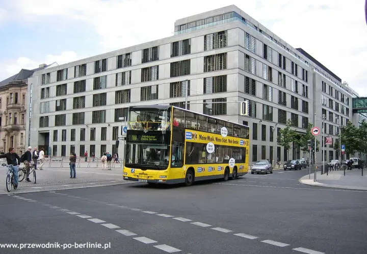 Żółte piętrowe autobusy kursują po Berlinie, mijając nowoczesne budynki.
