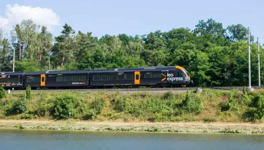Czarny pociąg Leo Express jedzie wzdłuż zielonego brzegu. Zastanawiasz się, ile kosztuje bilet z Warszawy do Krakowa?