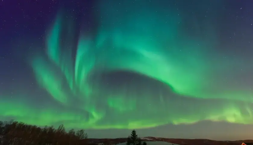 Zielona zorza polarna nad śnieżnym krajobrazem w Norwegii. Niebo rozświetlone tańczącymi światłami.