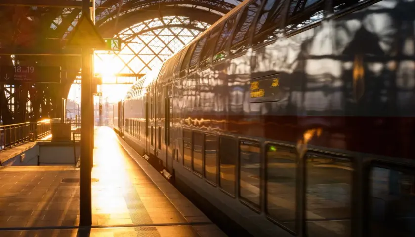 Złote światło wschodu słońca oświetla peron i pociąg PKP. Widok na dworzec kolejowy z pociągiem dwupoziomowym.