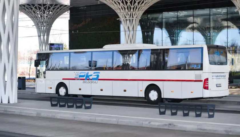 Biały autobus PKS Biłgoraj na nowoczesnym dworcu autobusowym z zieloną ścianą i futurystycznym zadaszeniem.