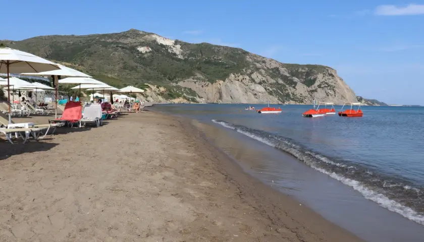 Słoneczny dzień na plaży Kalamaki. Leżaki pod parasolami, spokojne morze i czerwone rowery wodne.