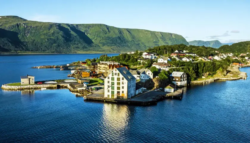 Malowniczy widok na Ålesund Vigra z domkami nad wodą i zielonymi wzgórzami w tle.