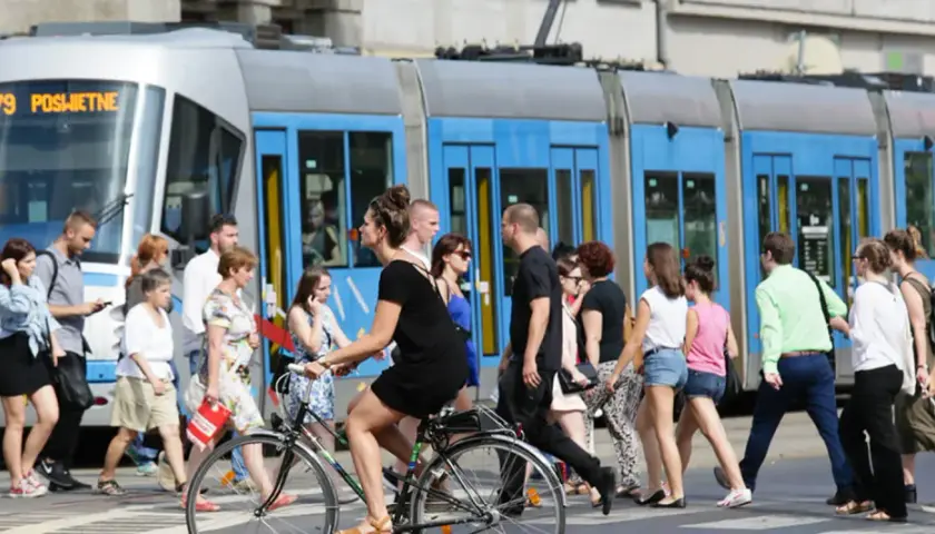 Ludzie przechodzą przez pasy, obok tramwaju z napisem "79 POŚWIETNE". To typowy widok wrocławskiego kod boczny pojazdu.