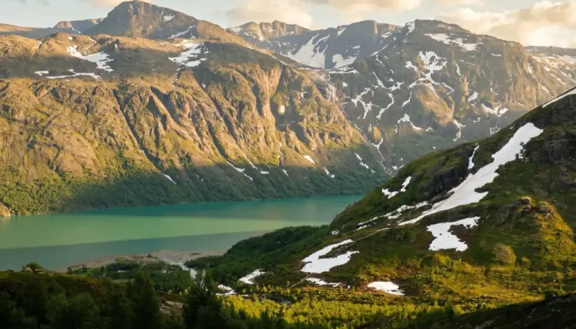 Majestatyczne góry Jotunheimen, jezioro o turkusowej barwie i zielone zbocza z resztkami śniegu.