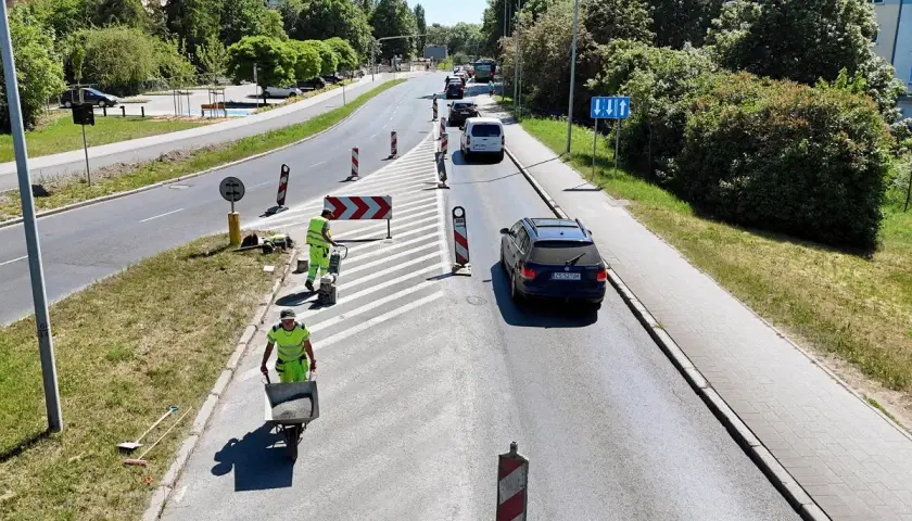 Prace drogowe na linii 101 w Szczecinie. Robotnicy w kamizelkach odblaskowych układają nawierzchnię, jeden z nich pcha taczkę z materiałem.