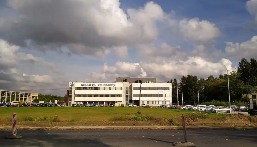 Szpital im. Św. Rodziny, dojazd autobusem. Budynek szpitala z parkingiem i zielenią.