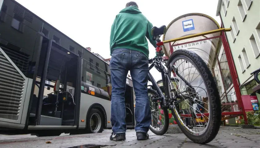 Mężczyzna z rowerem czeka na autobus. Rower stoi obok niego przy przystanku.