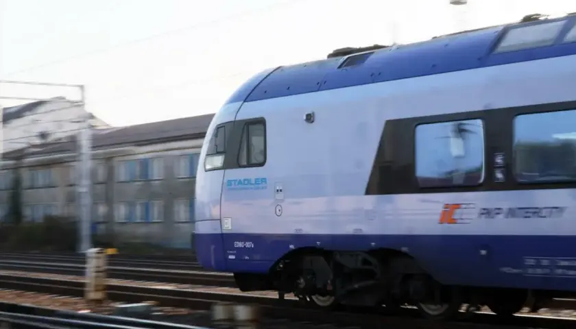 Pociąg PKP Intercity Stadler ED160-007 mija budynek. Może to być początek podróży lub zwrot biletu PKP.