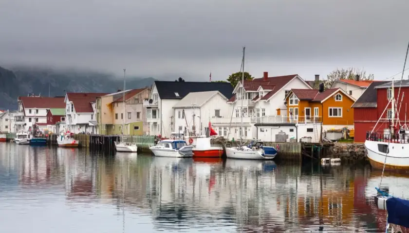 Kolorowy port w Norwegii z domkami i łodziami odbijającymi się w spokojnej wodzie.
