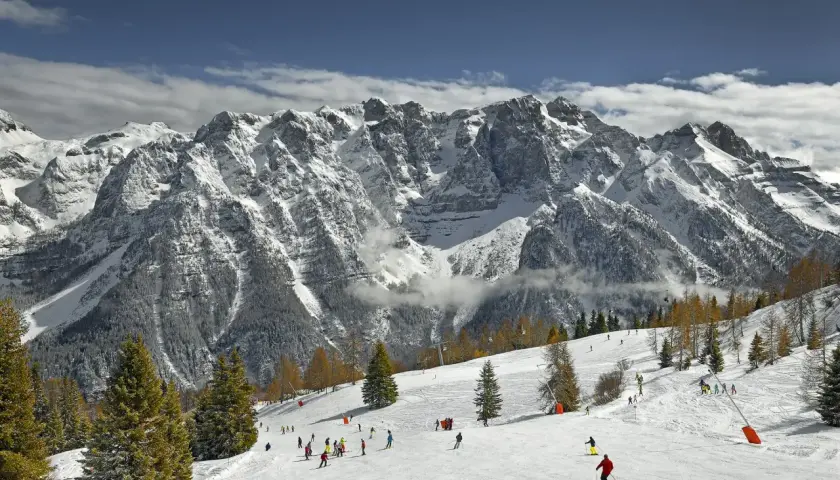 Narciarze szusują po ośnieżonych stokach w Marilleva, pod majestatycznymi, skalistymi szczytami Dolomitów.
