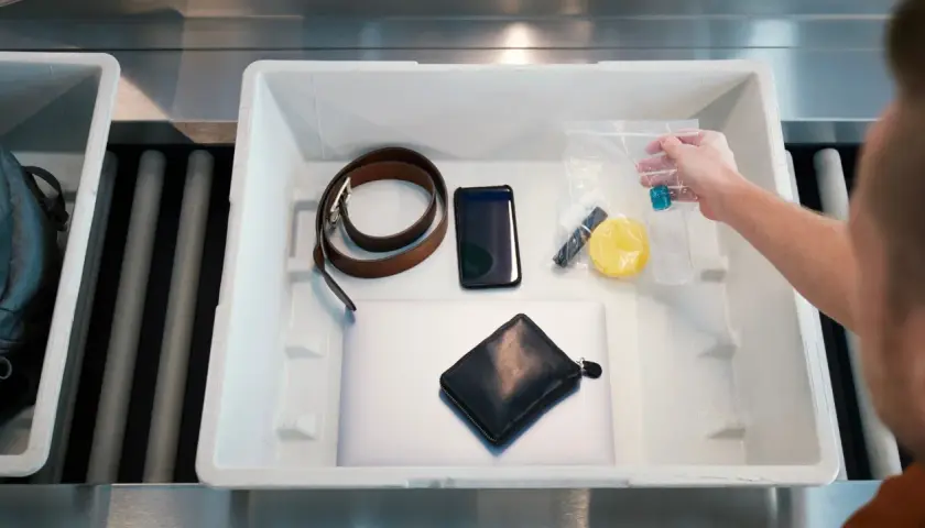 Co wykrywają papierki na lotnisku? Na taśmie leżą: laptop, portfel, telefon, pasek, kosmetyczka z płynami i inne drobiazgi.
