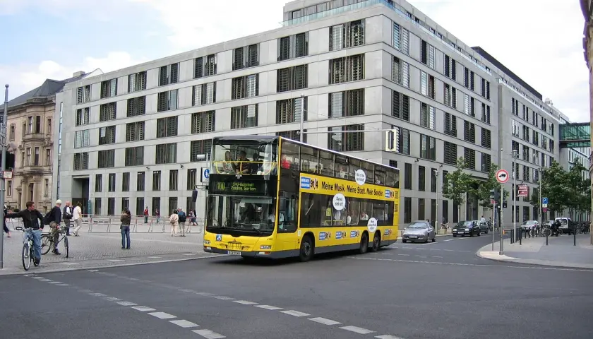 Żółte piętrowe autobusy kursują po Berlinie, mijając nowoczesne budynki.
