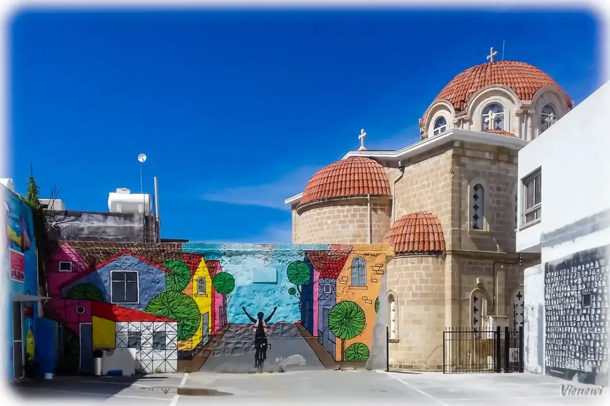 Kolorowy mural z rowerzystą i domkami na tle kościoła z kopułami. Pafos stare miasto.