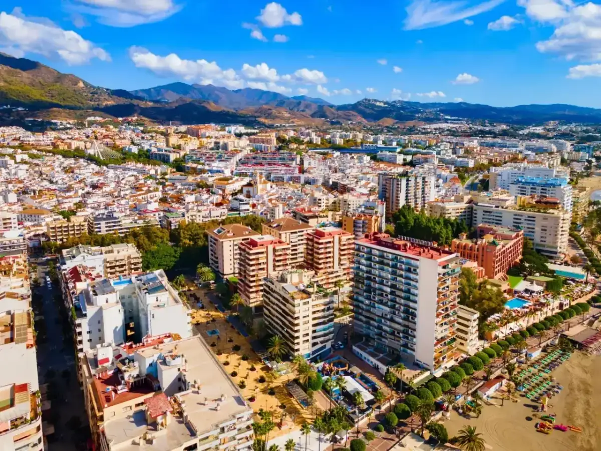 Widok z lotu ptaka na słoneczne miasto Malaga Marbella, z górami w tle i plażą pełną leżaków.