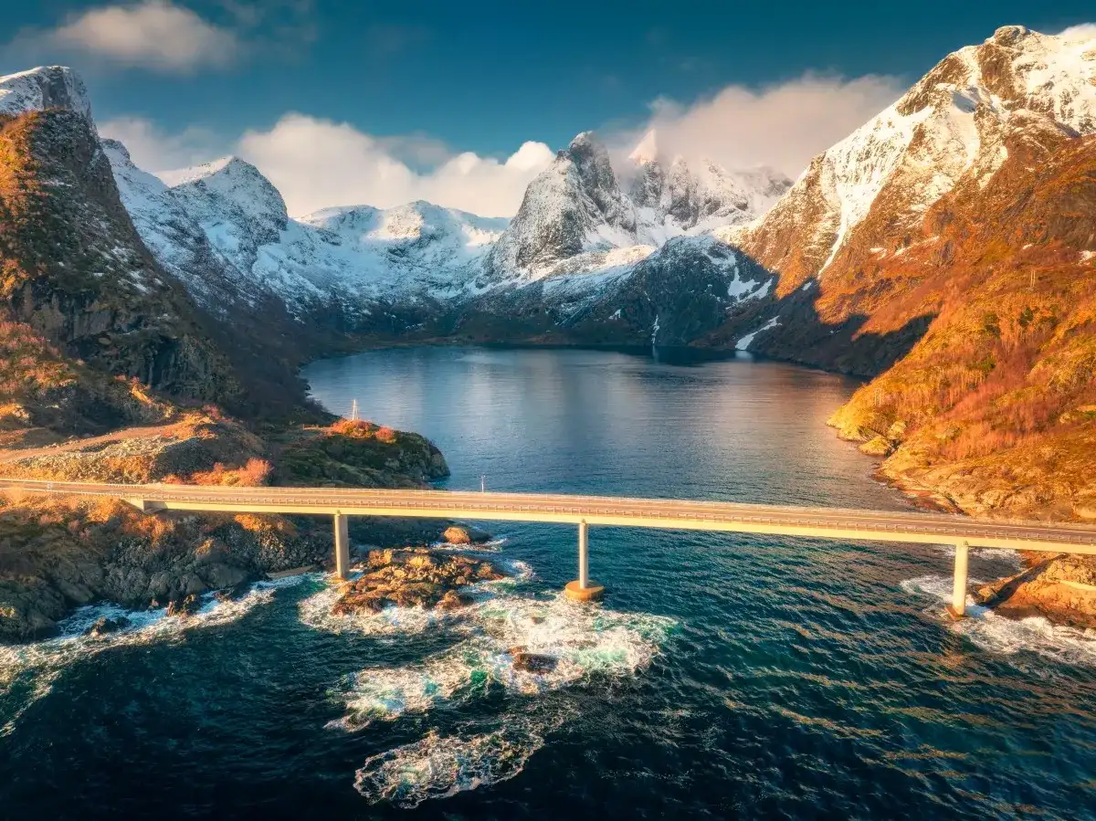Most majestatyczny fiord w Norwegii, z mostem przecinającym turkusową wodę i ośnieżonymi górami w tle.