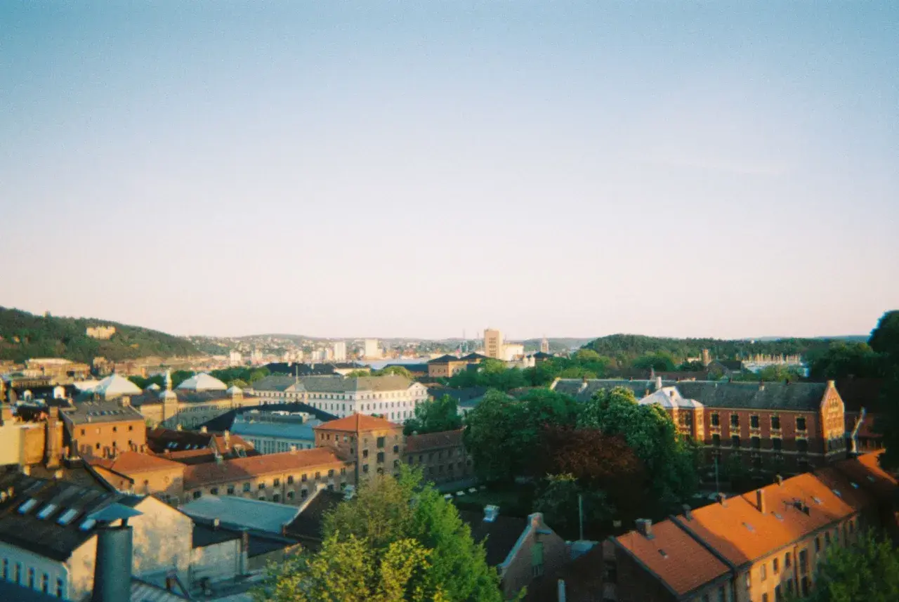 Widok na centrum Oslo z dachu kamienicy. Słońce zachodzi nad miastem, rzucając ciepłe światło na dachy i fasady budynków.