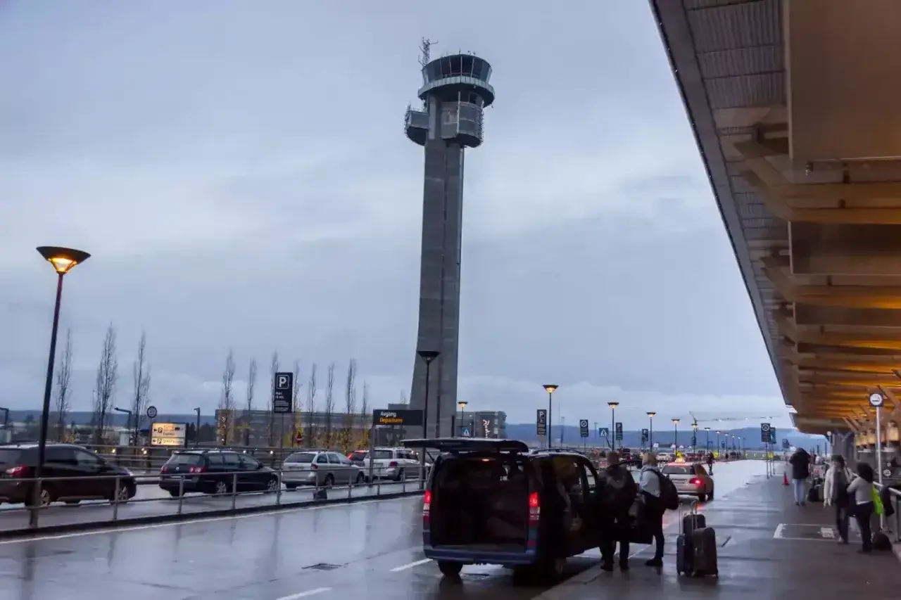 Wieża kontrolna na lotnisku w Norwegii. Samochody i ludzie przy terminalu, deszczowa pogoda.