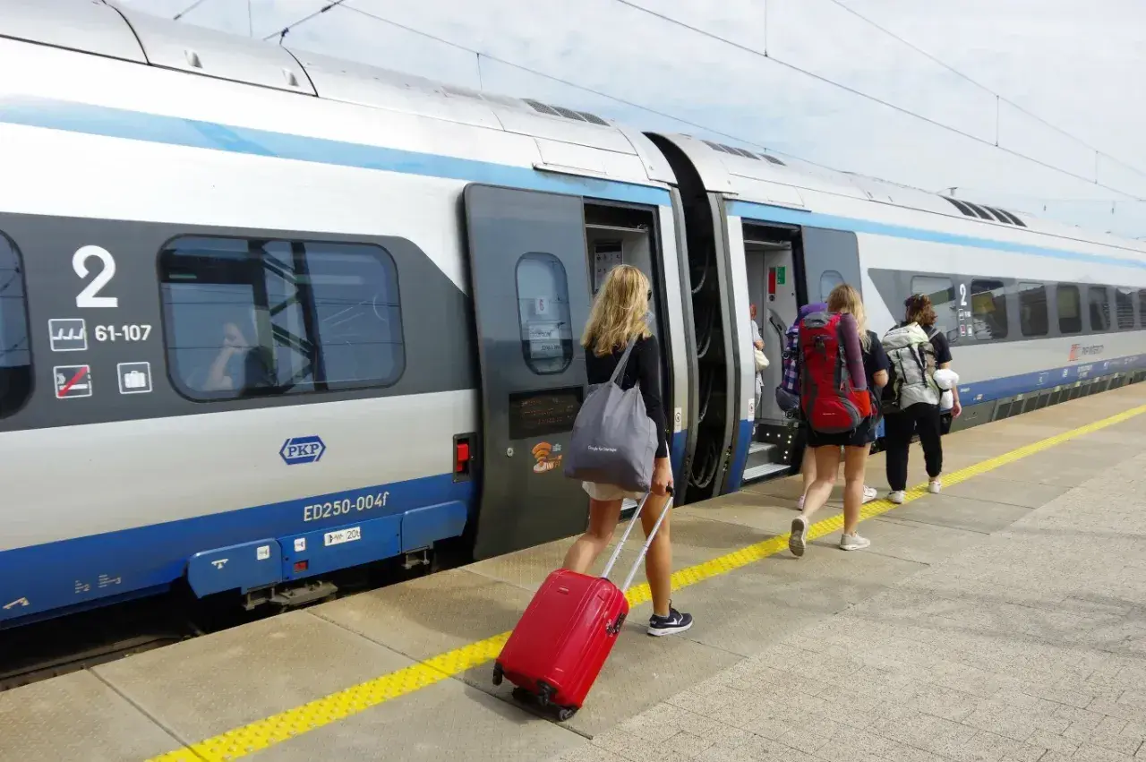 Dziewczyny z plecakami i walizką wsiadają do pociągu PKP. Warto wiedzieć, jak kupić bilet na pociąg, by podróżować bez stresu.