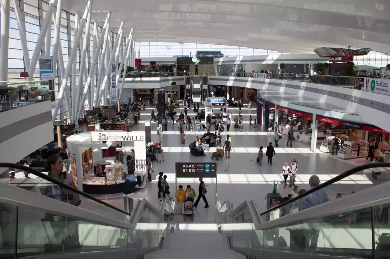 Tętniący życiem terminal lotniska w Budapeszcie, z ludźmi poruszającymi się po sklepach i kawiarniach, gotowi na transport z lotniska.