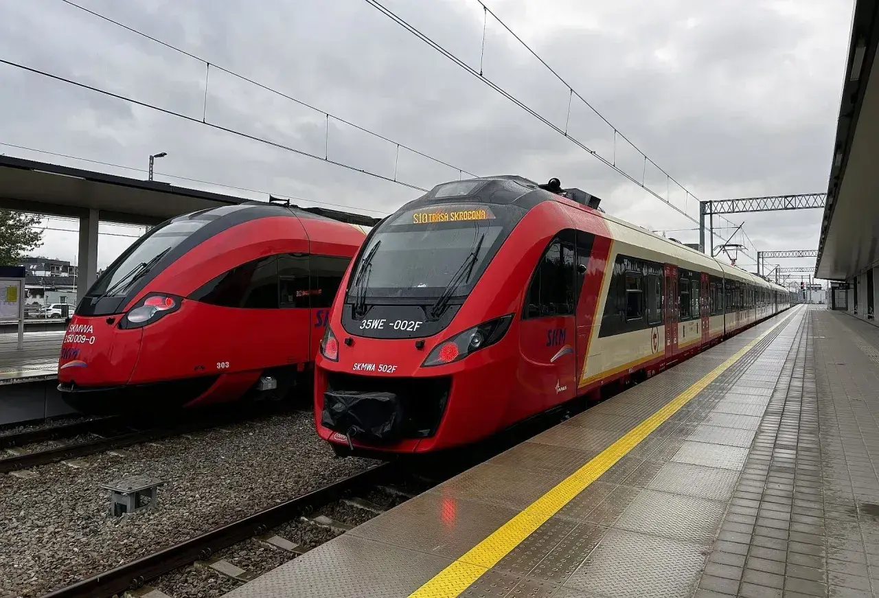 Dwa czerwone pociągi SKM stoją na stacji. Jeden z nich ma na wyświetlaczu informację "SKM Trasa Skrócona", sugerując przebookowanie.