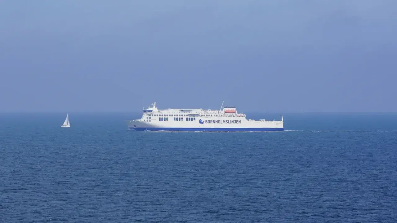 Prom, który ułatwia dojazd z Polski, płynie po spokojnym morzu. Obok żaglówka.