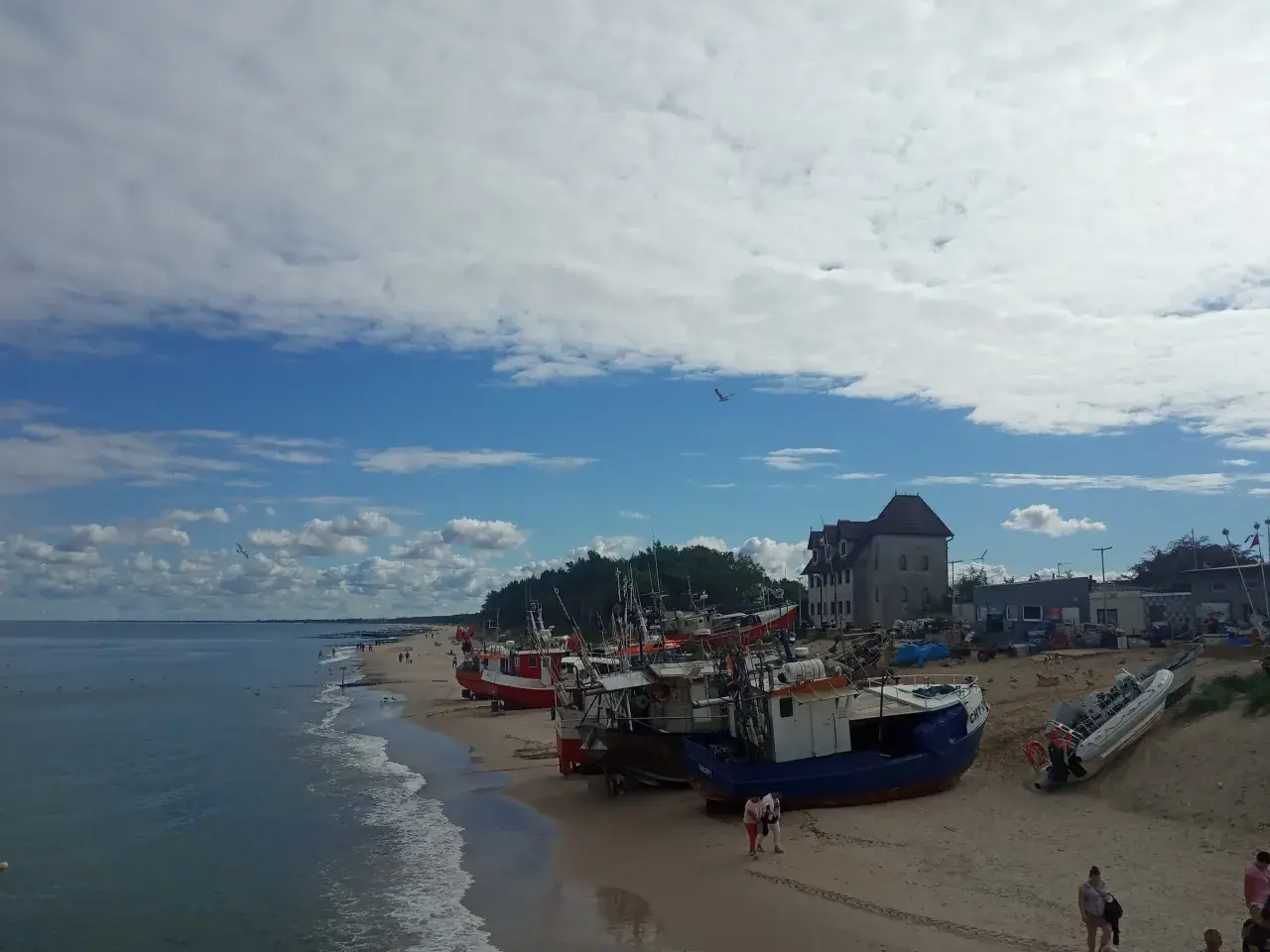 Chłopy atrakcje: łodzie rybackie na plaży, morze i budynki w tle.