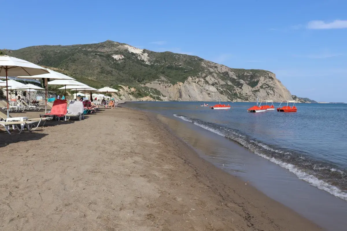 Słoneczny dzień na plaży Kalamaki. Leżaki pod parasolami, spokojne morze i czerwone rowery wodne.