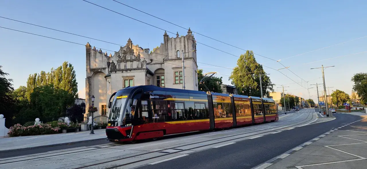 Nowoczesny tramwaj pabianice z czerwono-żółtymi pasami jedzie w stronę zabytkowego budynku.
