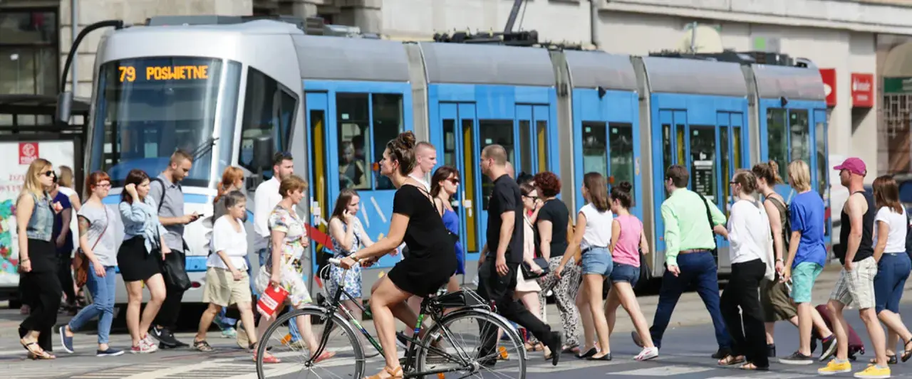 Ludzie przechodzą przez pasy, obok tramwaju z napisem "79 POŚWIETNE". To typowy widok wrocławskiego kod boczny pojazdu.
