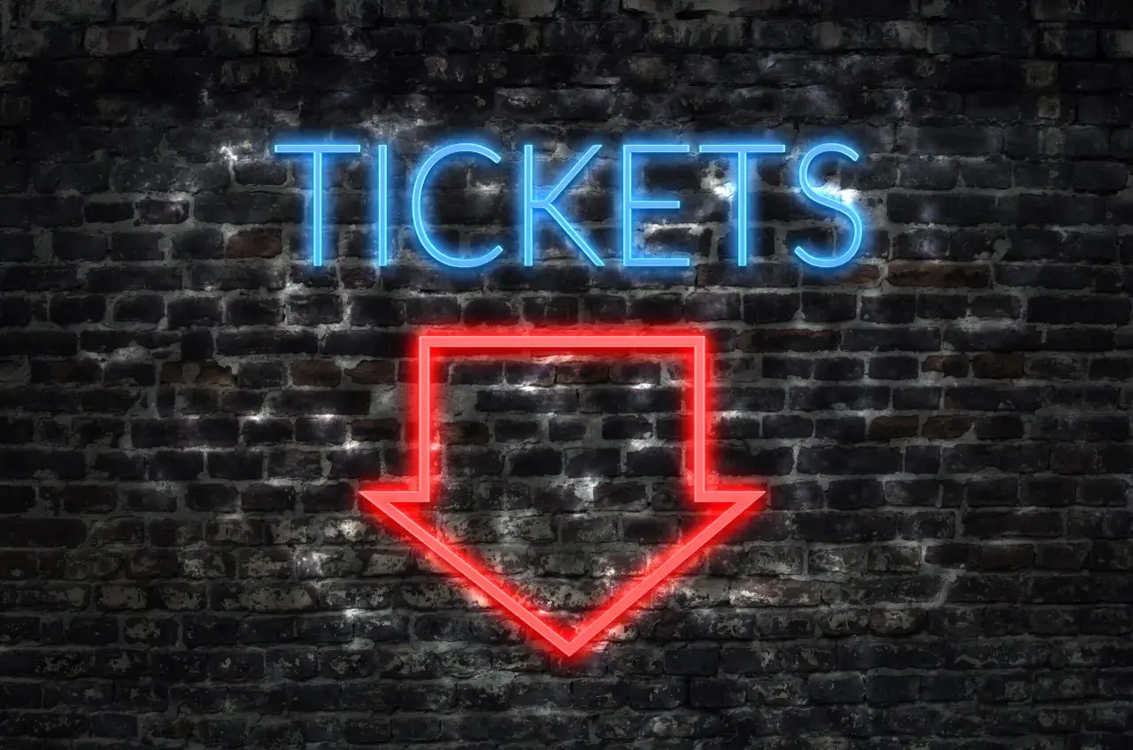 Napis "TICKETS" świeci na niebiesko nad czerwoną strzałką wskazującą w dół. To znak, jak kupić bilet online.