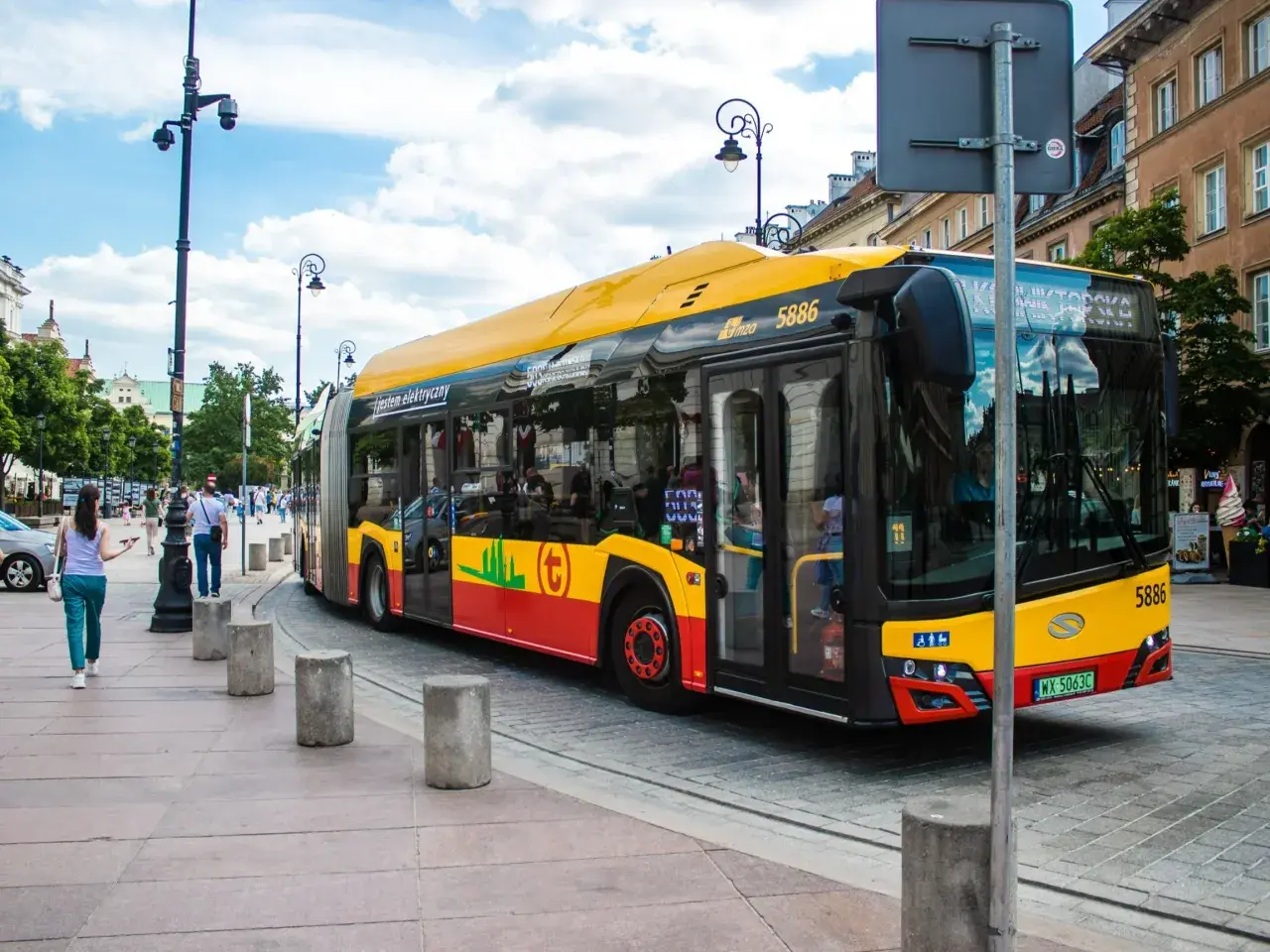 Żółto-czerwony autobus miejski, symbol darmowej komunikacji miejskiej, jedzie ulicą.