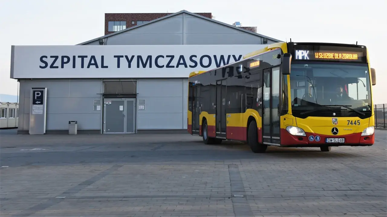 Żółto-czerwony autobus MPK z napisem "W SŁUŻBIE DLA ZDROWIA" dojeżdża do Szpitala Tymczasowego we Wrocławiu przy ul. Borowskiej.