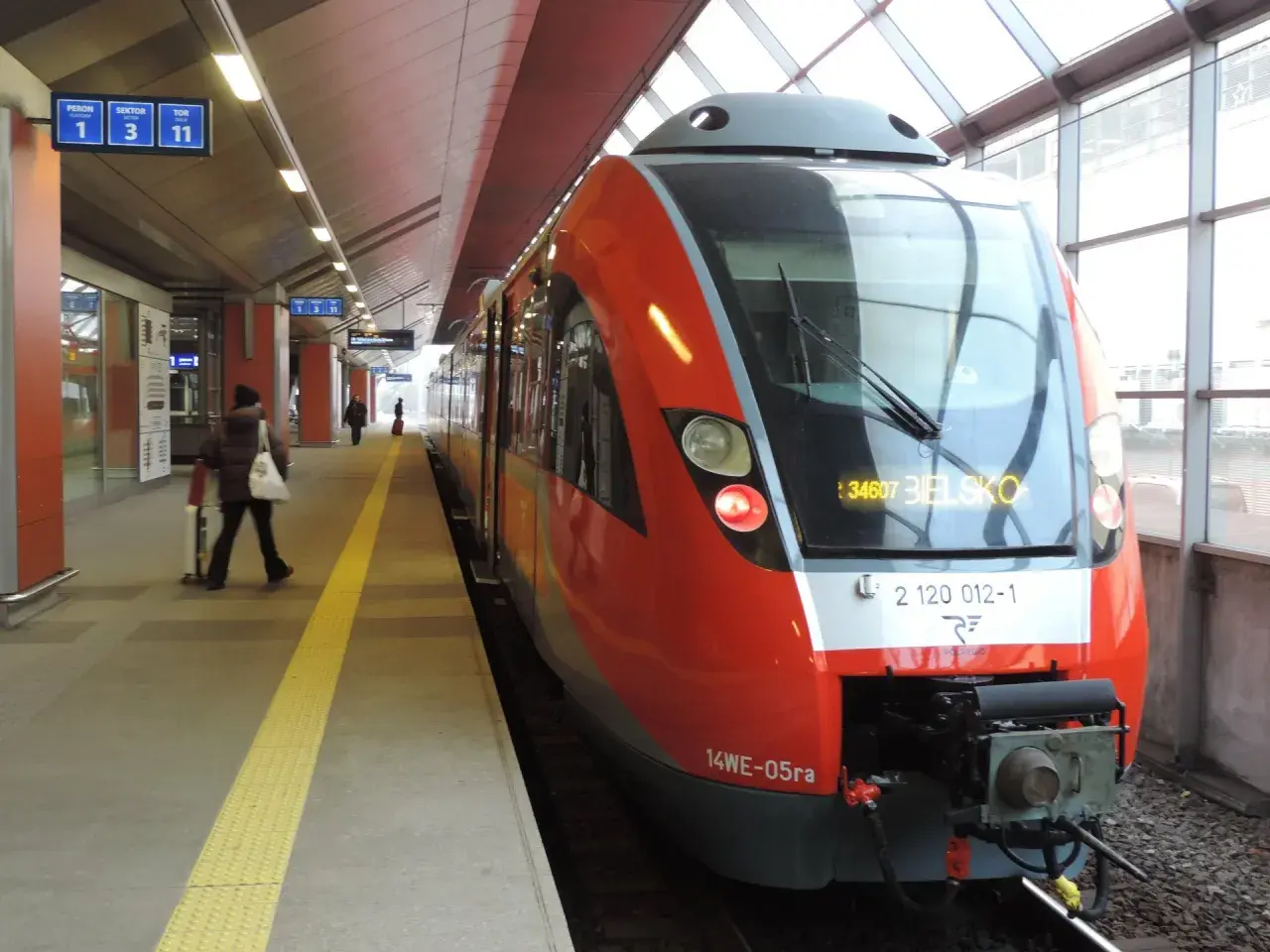 Czerwony pociąg na stacji, gotowy do odjazdu. Sprawdzam rozkład jazdy, by wybrać najlepszą taryfę małopolską.