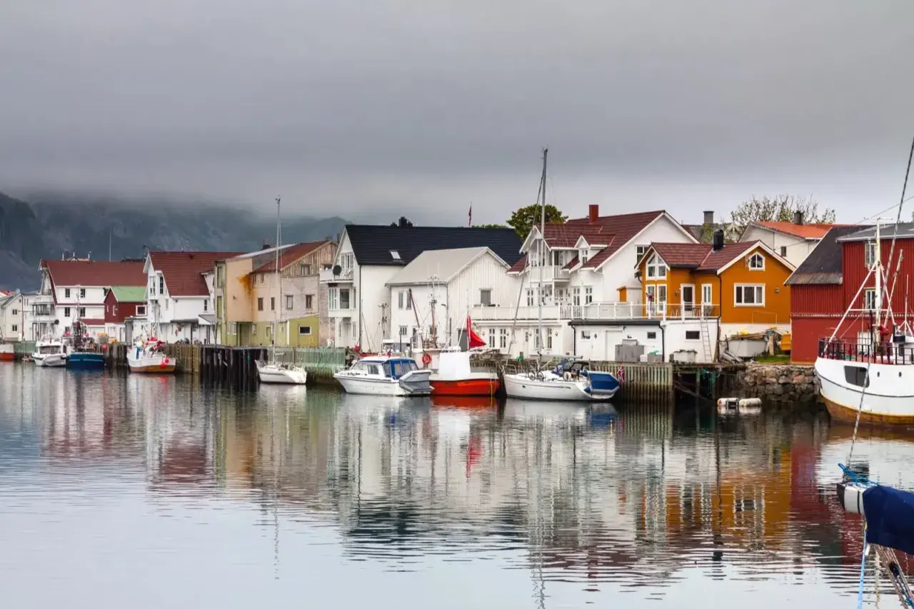 Kolorowy port w Norwegii z domkami i łodziami odbijającymi się w spokojnej wodzie.