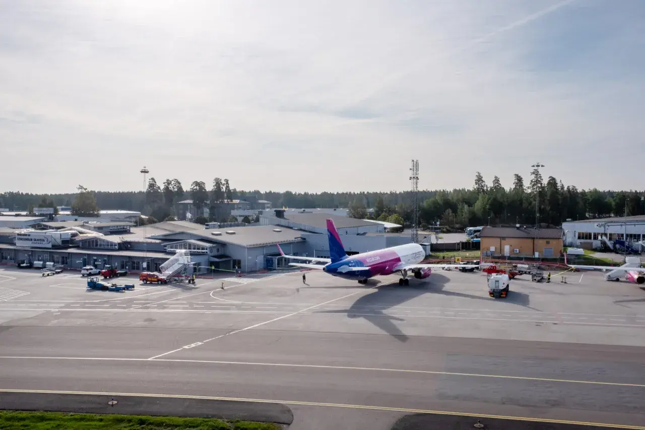 Samolot Wizz Air na płycie lotniska Sztokholm Skavsta. W tle budynki terminali i wieża kontroli lotów.