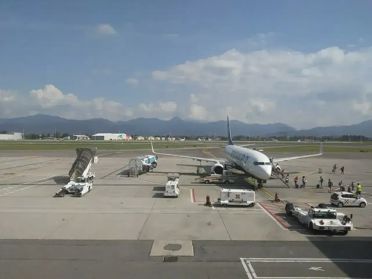Samolot Ryanair na lotnisku Orio al Serio, pasażerowie wsiadają. W tle góry i chmury.