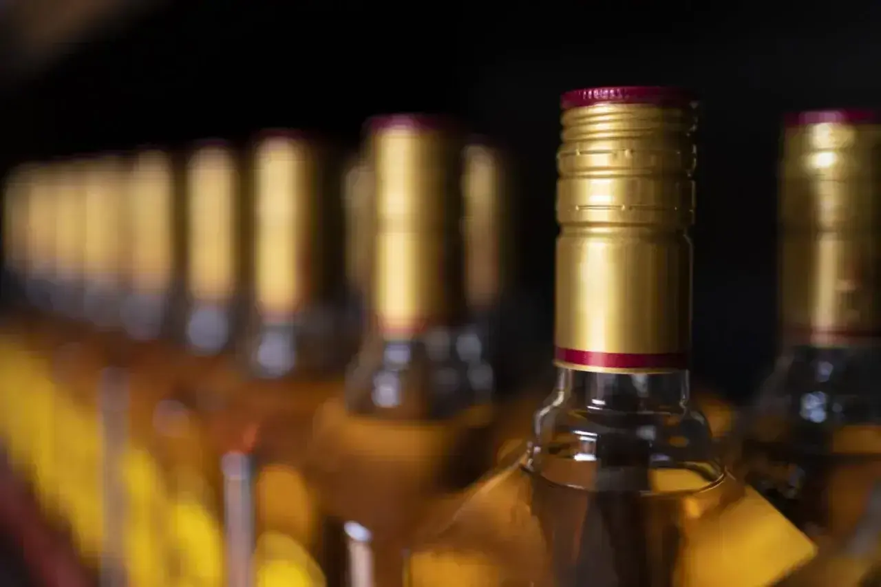 Rząd butelek z bursztynowym płynem, każda z złotą zakrętką i czerwoną obrączką. Zastanawiasz się, ile alkoholu do uk?