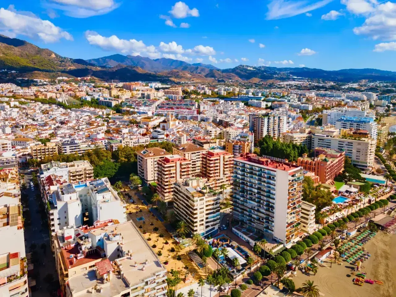 Widok z lotu ptaka na słoneczne miasto Malaga Marbella, z górami w tle i plażą pełną leżaków.