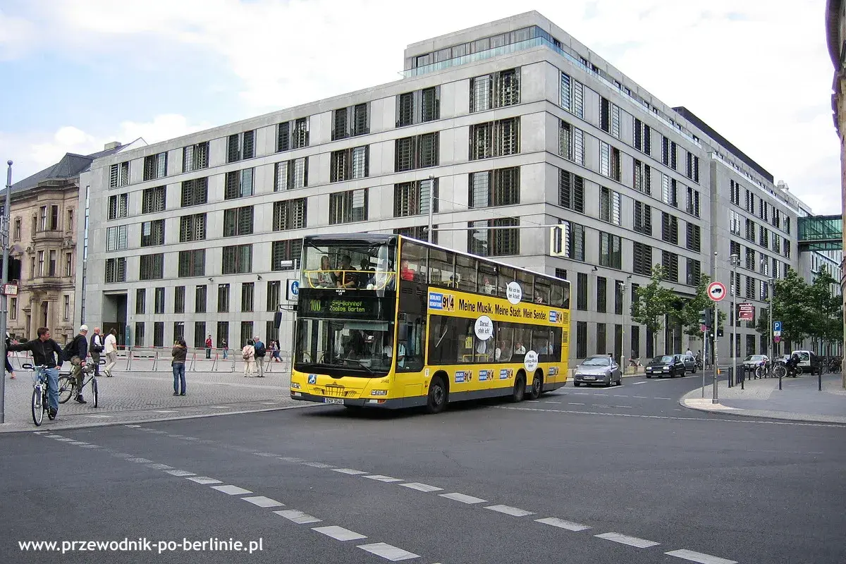 Żółte piętrowe autobusy kursują po Berlinie, mijając nowoczesne budynki.