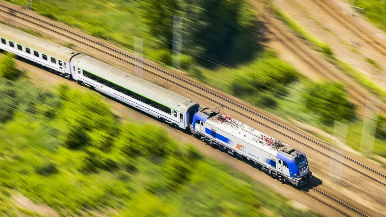 Pociąg PKP Intercity pędzi przez zielone krajobrazy. Szybko kupisz bilet na podróż przez aplikację do zakupu biletów PKP.