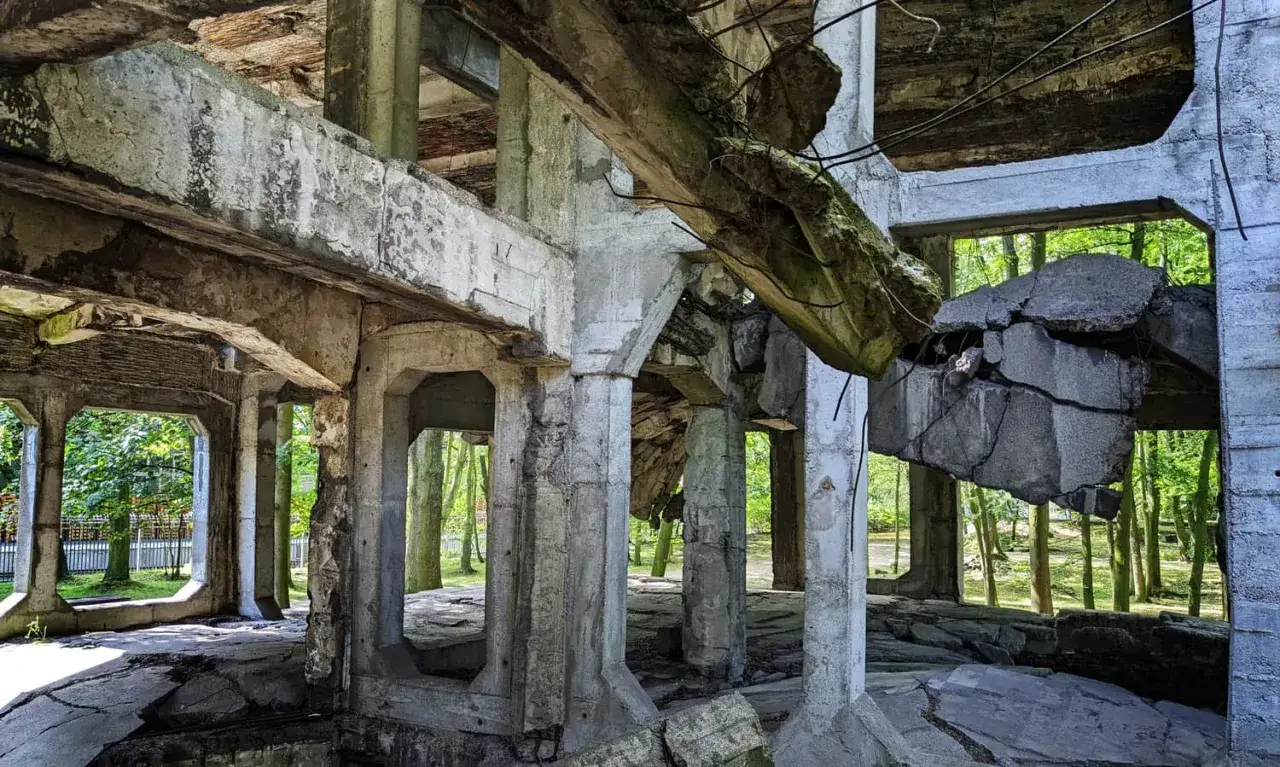 Ruiny koszar na Westerplatte podczas zwiedzania. Zniszczone betonowe konstrukcje, zawalone stropy i zielone drzewa w tle.