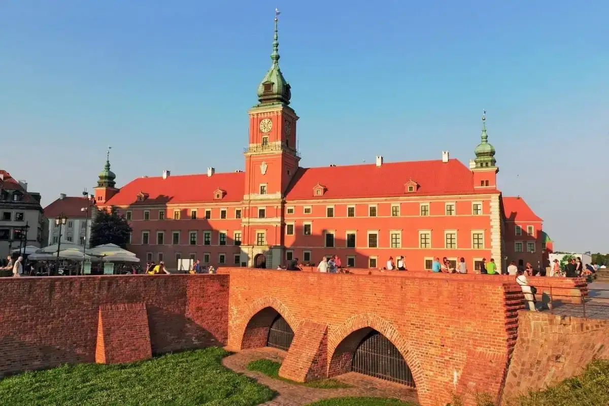 Zamek Królewski w Warszawie, część trasy po Starym Mieście, z mostem i ludźmi odpoczywającymi na murze.