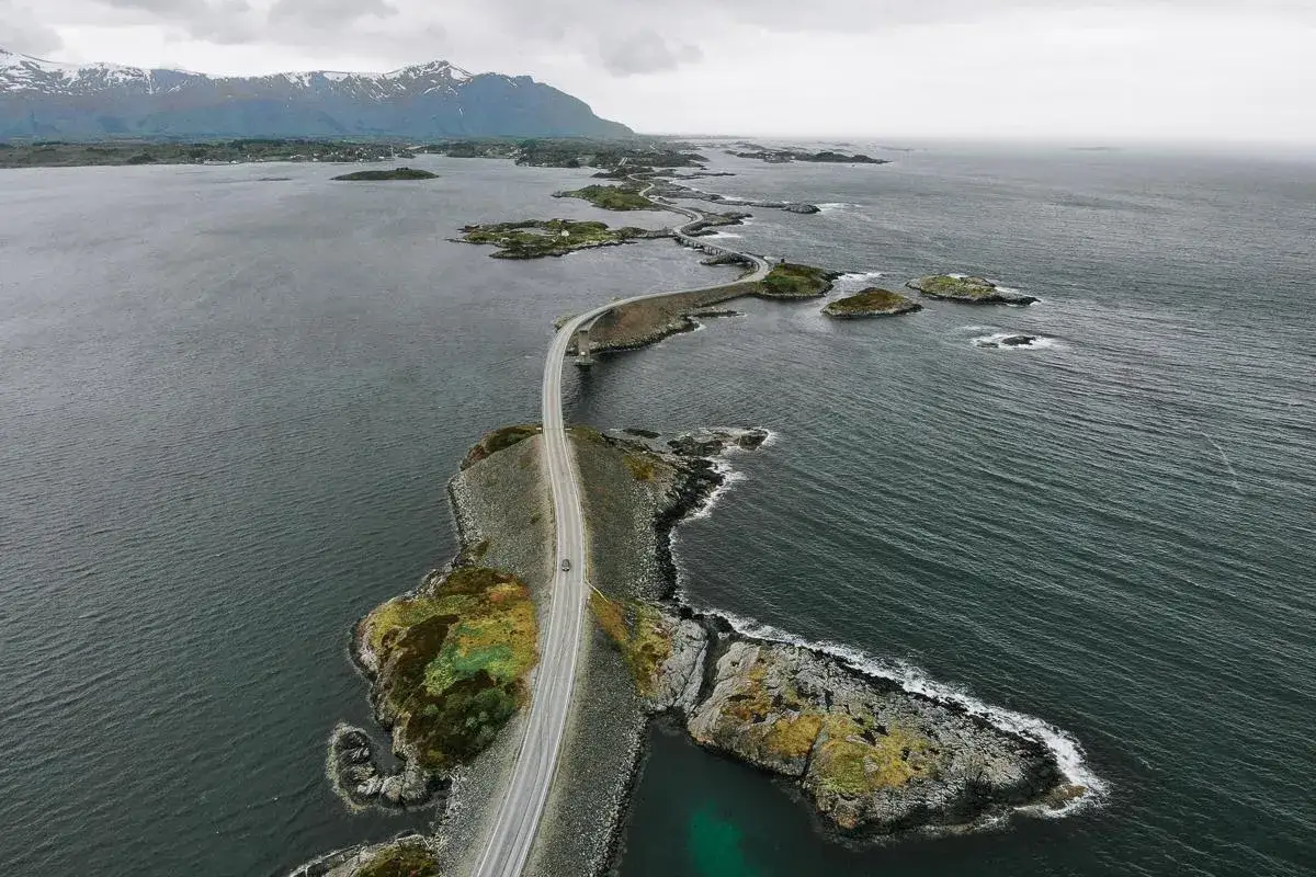 Droga wijąca się między wysepkami na wzburzonym morzu. Atlantic Ocean Road, z górami w tle, wygląda jak szlak łączący światy.