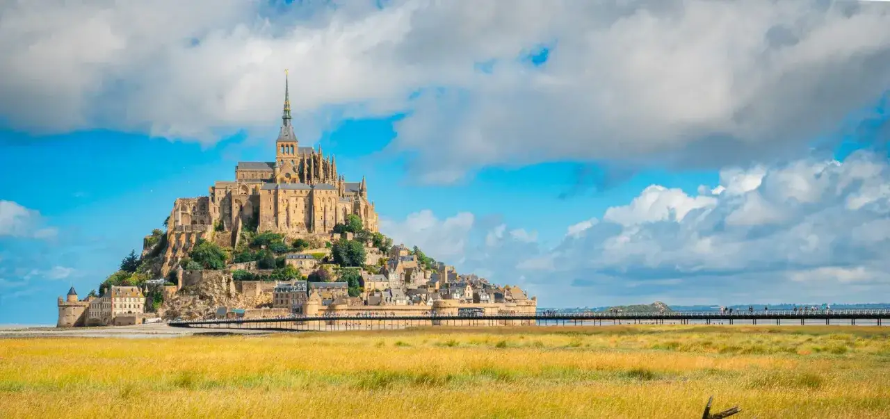 Majestatyczny Le Mont Saint-Michel, średniowieczny klasztor na skalistej wyspie, góruje nad otaczającymi go polami i mostem.
