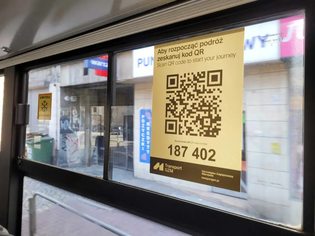 Na szybie autobusu wisi żółta kartka z dużym kodem QR i napisem 