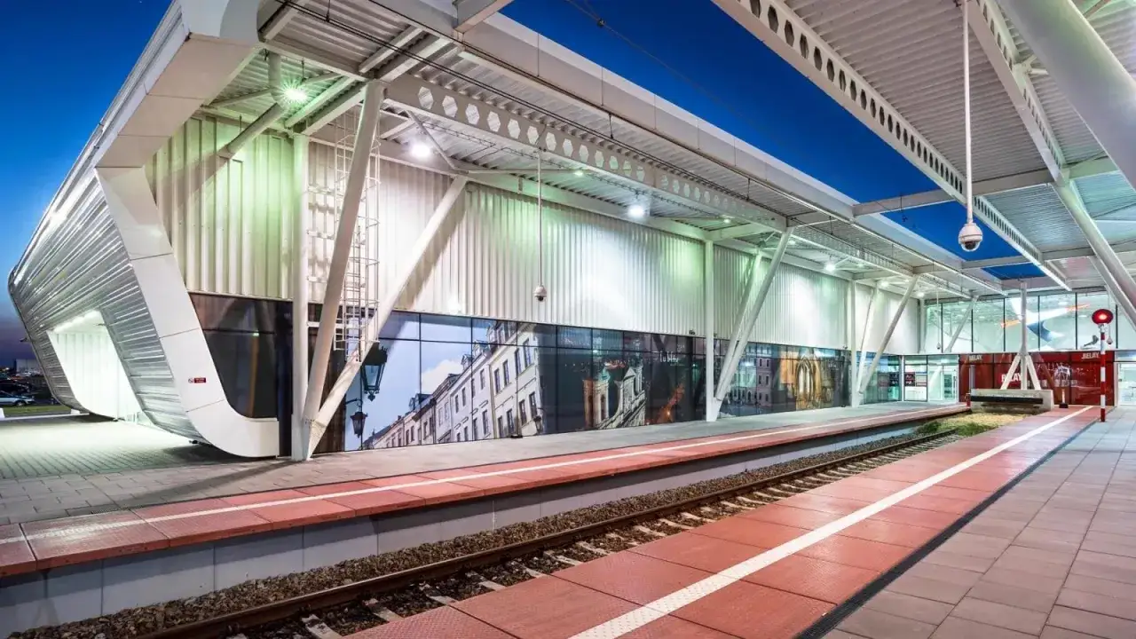 Nowoczesna stacja, gdzie szynobus Lublin Lotnisko czeka na pasażerów. Futurystyczna architektura i widok na zabytkowe kamienice.